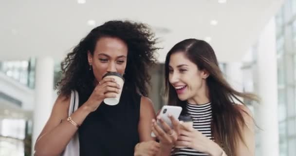 Coffee breaks are for catch ups. 4k video footage of young businesswomen chatting and using a smartphone while walking in an office on a coffee break. — Stockvideo