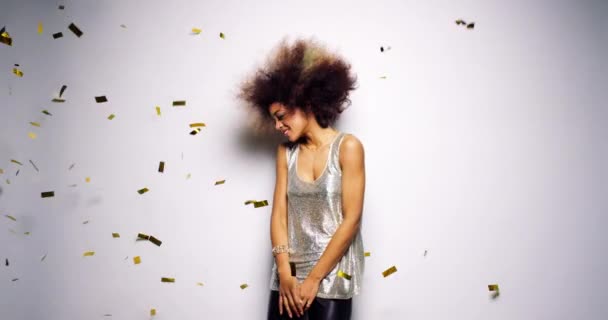 Carefree woman shaking her afro and having fun dancing against a white background at a party while gold confetti falls. Gold confetti falling as happy young African American woman dances — Stock video