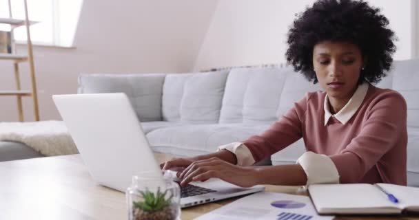 Afstandswerkers zijn in opkomst. 4k beeldmateriaal van een aantrekkelijke jonge vrouw met behulp van een laptop tijdens het werken thuis. — Stockvideo