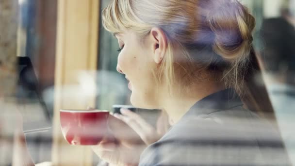 Egy boldog üzletasszony kávézik egy kávézóban, miközben a vezeték nélküli tabletjét használja. Egy fiatal nő ül egy kávézóban, nézegeti a digitális tabletjét, és iszik egy csésze teát.. — Stock videók