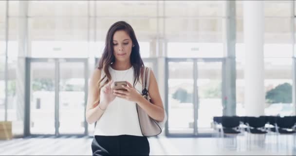Los conectados son mejores en mantenerse al día con el ritmo de los negocios. Imágenes de video de 4k de una joven empresaria usando un teléfono celular mientras camina en una oficina moderna. — Vídeo de stock