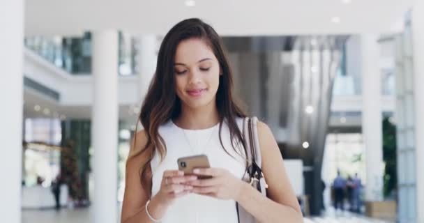 Siempre está al tanto de sus objetivos. Imágenes de video de 4k de una joven empresaria usando un teléfono celular mientras camina en una oficina moderna. — Vídeo de stock