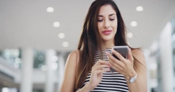 Conectado a una comunidad de negocios en línea. Imágenes de video 4k de una joven empresaria usando un teléfono inteligente mientras camina a través de una oficina moderna. — Vídeo de stock