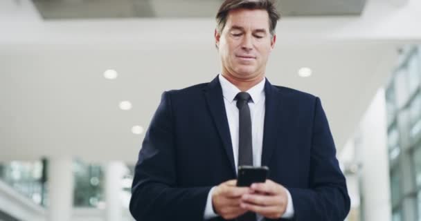 Mantém-te ligado, fica preparado. Filmagem em vídeo 4k de um empresário maduro usando um smartphone enquanto caminha por um escritório moderno. — Vídeo de Stock