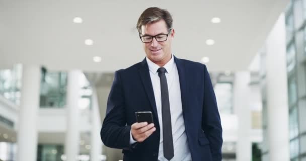 Conéctese al éxito. Imágenes de video 4k de un hombre de negocios maduro usando un teléfono inteligente mientras camina a través de una oficina moderna. — Vídeos de Stock