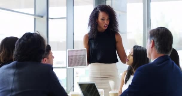 Presenting key notes to her team. 4k video footage of a businesswoman using a digital tablet while giving a presentation to her colleagues in an office. — Wideo stockowe