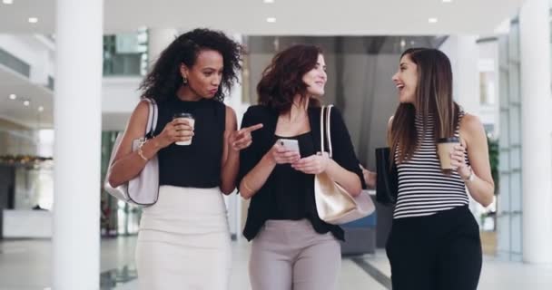 Bazen iş arkadaşları, her zaman arkadaşlar. 4K video görüntüleri, genç iş kadınlarının bir kahve molasında ofiste yürürken sohbet ve akıllı telefon kullanmalarını gösteriyor.. — Stok video