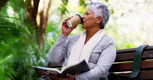 Getting a nice read in for the day. 4k video footage of a mature woman drinking coffee while reading a book in the park. — Stock Video