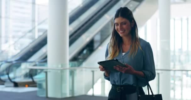 Working on the move. 4k video footage of an attractive young businesswoman using her tablet while walking through her office building. — Wideo stockowe