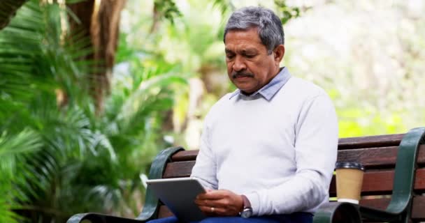 Dieser Großvater hat keine Angst vor ein wenig Technologie. 4k Videomaterial eines reifen Mannes, der ein digitales Tablet benutzt, während er auf einer Bank im Park sitzt. — Stockvideo