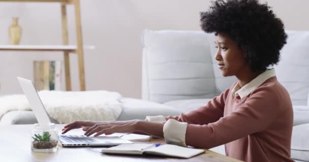 Ze runt haar eigen zaak als een baas. 4k beeldmateriaal van een aantrekkelijke jonge vrouw met behulp van een laptop en het maken van notities tijdens het werken thuis. — Stockvideo