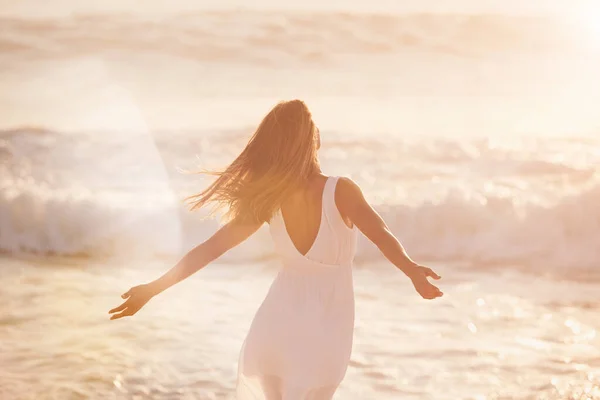 Uma jovem mulher aproveitando seu tempo na praia. Mulher despreocupada desfrutando do sol na praia. Parte de trás de uma mulher de conteúdo despreocupado comemorando e apreciando o pôr do sol na praia — Fotografia de Stock