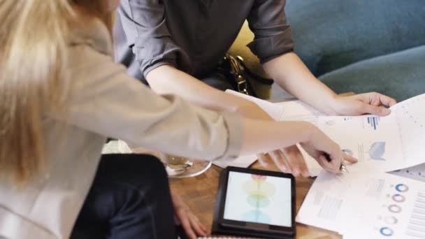 Due donne d'affari che leggono documenti finanziari durante una riunione mentre utilizzano un tablet wireless. Due colleghi di lavoro collaborano e pianificano durante una riunione mentre parlano e leggono documenti in un caffè — Video Stock