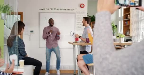 A group of diverse businesspeople clapping and cheering while a coworker dances and is recorded on a cellphone. A carefree businessman dancing in front of his cheerful colleagues celebrating — Vídeo de stock