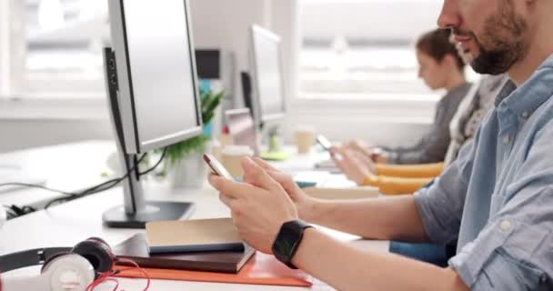 Diverse group of businesspeople sitting at their desks typing on computer keyboards and. sending text messages on cellphones. Professional corporate team working on tech devices at their desk in a row — Stockvideo