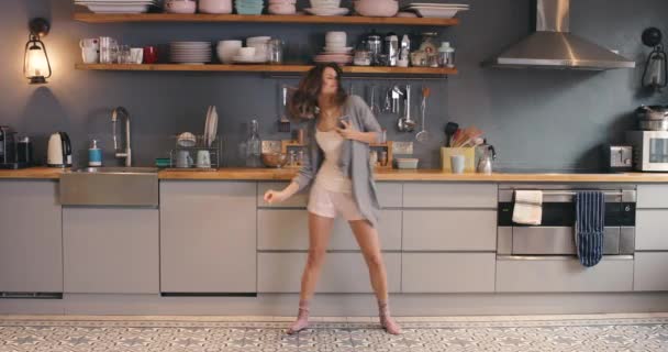 A young woman using a phone while dancing in the kitchen at home. A happy young woman using her cellphone and playfully dancing in her kitchen. Carefree woman having fun dancing in her apartment — стоковое видео