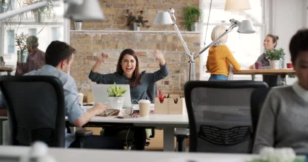 A group of diverse colleagues clapping for their excited coworker. A cheerful businesswoman working on her laptop, removing her earphones to celebrate her success. Corporate business team celebrating — Vídeo de stock