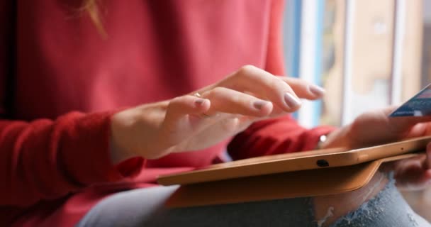Closeup of the hand of a woman using her wireless tablet, paying for online shopping purchases with her credit card. A woman browsing through a digital app on her wireless tablet. Woman at home — стоковое видео