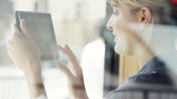 A young businesswoman scrolling through photos on her wireless tablet. A happy woman sitting in a cafe using her digital tablet to connect online. Young woman looking at photos on her tablet — Stock Video