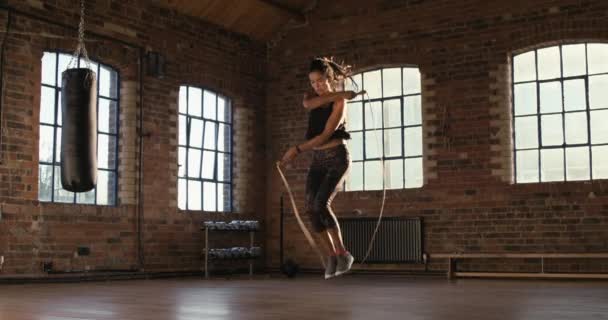 Серьёзная молодая женщина, прыгающая в спортзал. Молодая женщина работает над фитнесом, прыгает с скакалкой. Подходит для латиноамериканской женщины, занимающейся кардио и прыгающей в спортзал. Женщина прыгает с помощью скакалки — стоковое видео