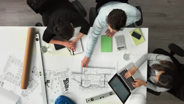 A group of architects calculating their finances using a building blueprint from above. A group of businesspeople talking about blueprints when brainstorming in a meeting using a laptop and calculator — Stok Video