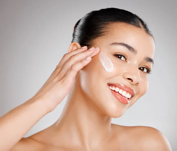 Manteniendo mi piel regordeta y sin poros. Foto de estudio de una atractiva joven que se aplica crema hidratante en la cara sobre un fondo gris. — Foto de Stock