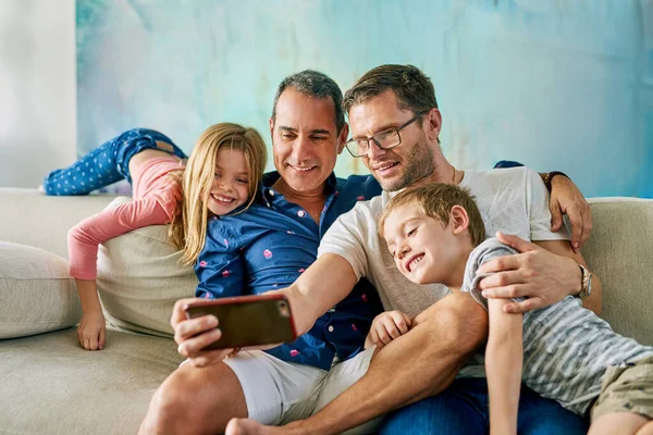 Ven aquí, nos estábamos tomando una selfie. Foto recortada de una familia cariñosa de cuatro tomando selfies en el sofá en casa. —  Fotos de Stock