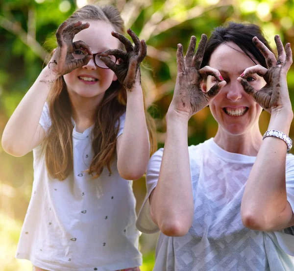 Play together. Stay together. Portrait of a mother and her little daughter covering their eyes with their muddy hands outside. — Stock Photo, Image
