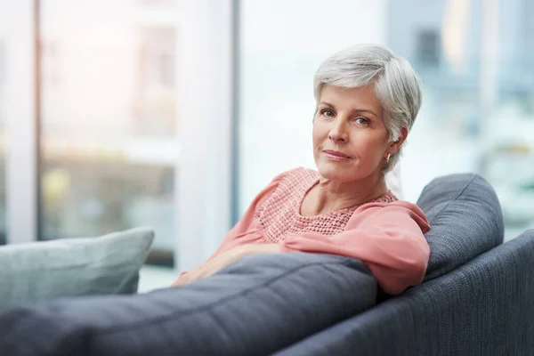 Always choose your own peace before anything else. Portrait of a cheerful mature woman relaxing on her sofa at home. — Stock Photo, Image