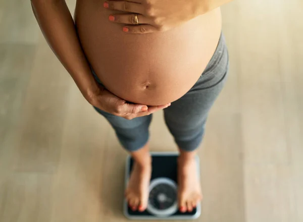 Těhotenství podle liber. Oříznutý vysoký úhel záběr těhotné ženy vážící se na stupnici. — Stock fotografie