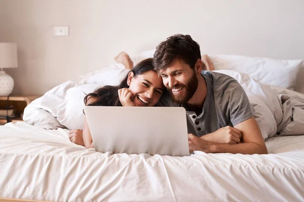 Algumas pessoas têm essa ligação especial. Tiro de um jovem casal feliz usando um laptop enquanto relaxa na cama em casa. — Fotografia de Stock