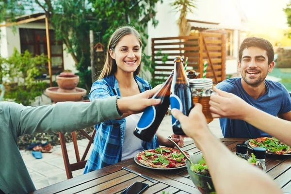 Comemore a vida com aqueles que você mais valoriza. Tiro de um grupo de jovens amigos segurando bebidas e brindes para celebrar sua amizade em torno de uma mesa ao ar livre. — Fotografia de Stock