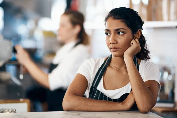 Kan en förändring i karriären vara på menyn. Skjuten av en ung kvinna som ser olycklig ut när hon arbetar bakom disken på ett kafé. — Stockfoto