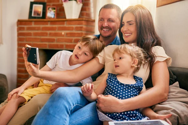 Najważniejszymi wspomnieniami są te z rodziną. Zdjęcie szczęśliwej młodej rodziny robiącej sobie selfie na kanapie w domu. — Zdjęcie stockowe