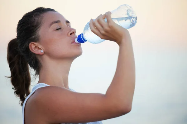 Trinken Sie mehr Wasser, Ihr Körper wird es Ihnen danken. Aufnahme einer sportlichen jungen Frau, die beim Laufen Wasser trinkt. — Stockfoto