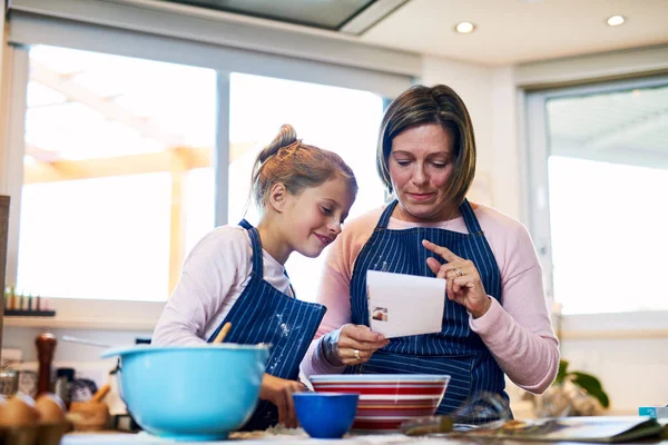 Eens kijken wat er op het recept staat... Shot van een moeder en haar dochtertje bakken samen thuis. — Stockfoto