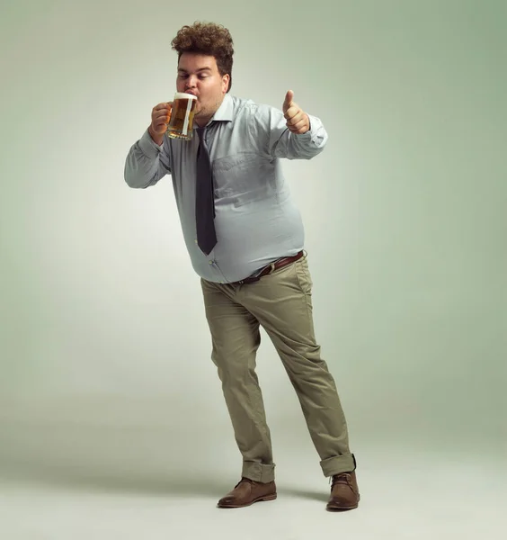 このビールは素晴らしい。ビールを飲みながら親指をあげる太りすぎの男のショット. — ストック写真
