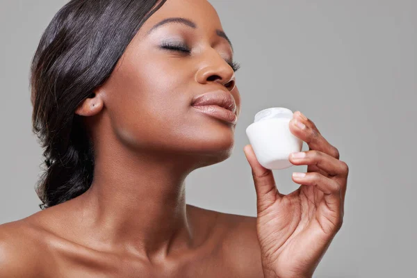 Youll be the envy of everyone with this.... Cropped studio shot of a beautiful young woman smelling her moisturizing cream. — Stock Photo, Image