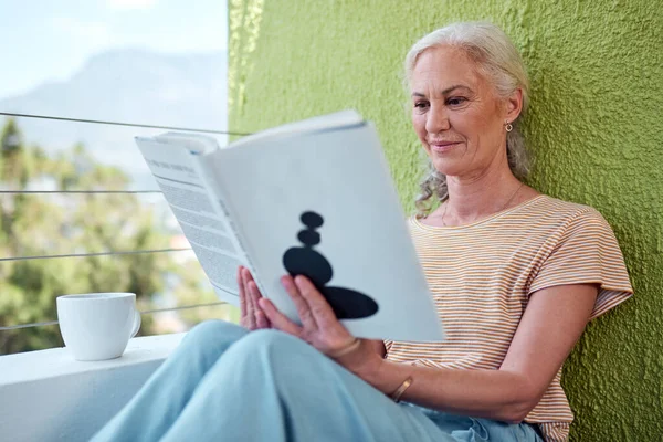 Tempo livre é para curling-se com um bom livro. Tiro de uma mulher madura lendo um livro e tomando café em sua varanda em casa. — Fotografia de Stock