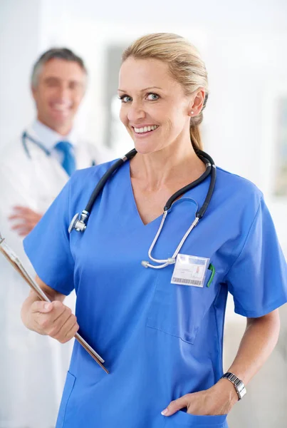 Estás en manos capaces. Retrato de una doctora en uniforme con un colega de pie en el fondo. —  Fotos de Stock