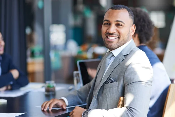 Ogni giorno realizziamo grandi cose in questo ufficio. Ritratto di un giovane uomo d'affari seduto in un ufficio con il collega sullo sfondo. — Foto Stock