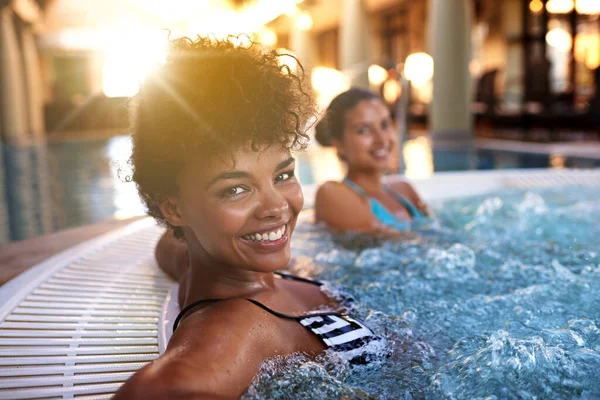 I migliori si divertono. Ritratto di una donna che si rilassa in una vasca idromassaggio con la sua amica sfocata sullo sfondo. — Foto Stock