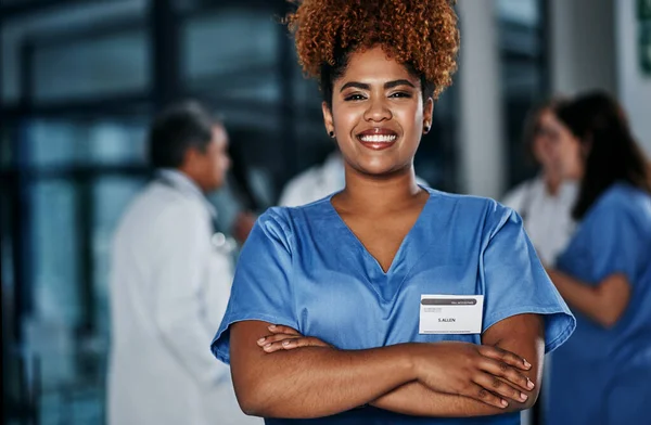 Mantendo sua saúde em mãos especializadas. Retrato de uma jovem médica confiante trabalhando em um hospital com seus colegas em segundo plano. — Fotografia de Stock