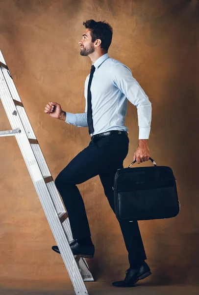 Вверх это единственный вариант. Студийный снимок красивого молодого бизнесмена, поднимающегося по лестнице на коричневом фоне. — стоковое фото