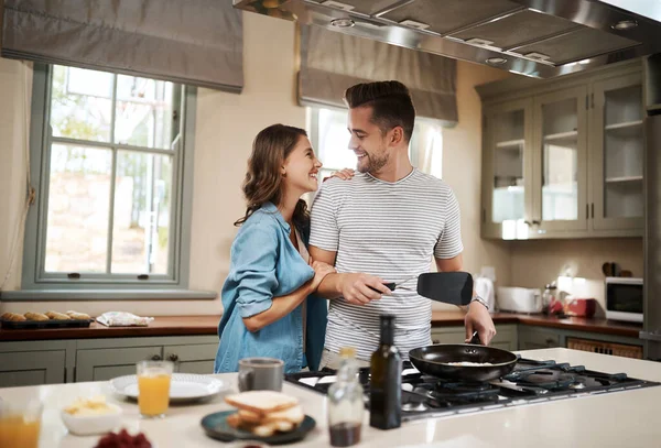 Probeer je wat brownie punten te scoren? shot van een jonge vrouw omarmen haar partner terwijl hij kookt ontbijt. — Stockfoto