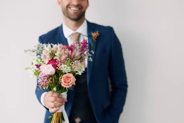 I fiori che le hanno conquistato il cuore. Studio foto di un bel giovane sposo che tiene un mazzo di fiori uno sfondo grigio. — Foto Stock