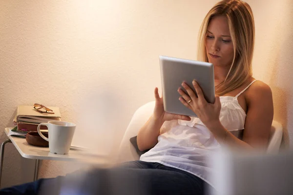 Selección de un nuevo libro electrónico para leer - Tablet digital. Mujer joven atractiva usando su tableta en un sillón en casa. — Foto de Stock