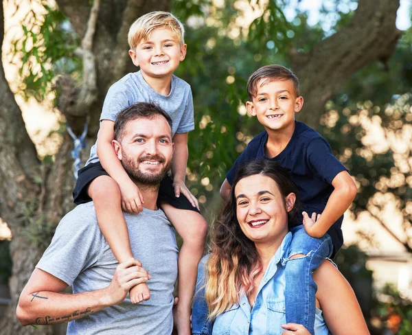 De mooiste ketting die mijn kinderen hebben. Portret van een prachtige familie met hun zonen op hun schouders in een park. — Stockfoto