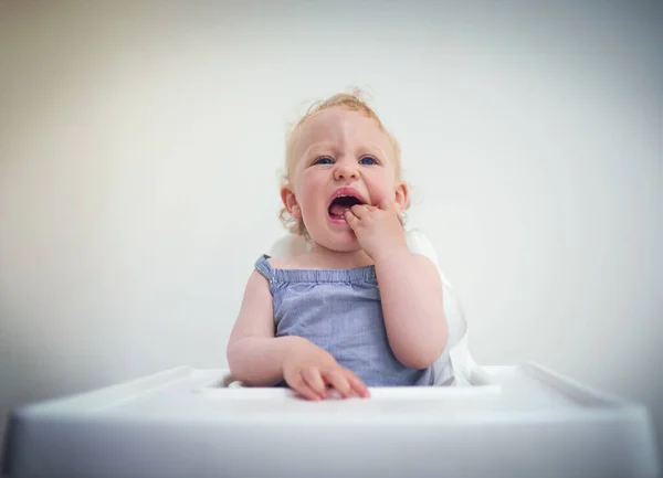 Yes, hands are tasty but how about some real food. Shot of an adorable baby girl sitting in her high chair at home. — Stock Photo, Image