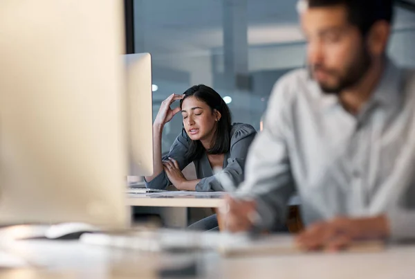 La stanchezza eccessiva porta a prestazioni insufficienti. Foto di una giovane donna che si sente stressata mentre usa un auricolare e un computer a tarda notte in un ufficio moderno. — Foto Stock